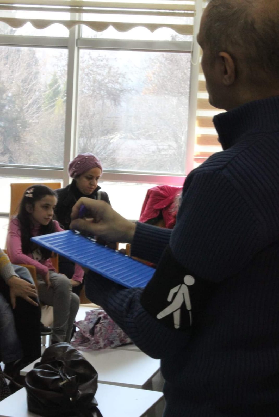 Fotoğrafta; Ali YILDIRIM braille yazı tabletini önünde bulunan iki öğrenciye gösteriyor.